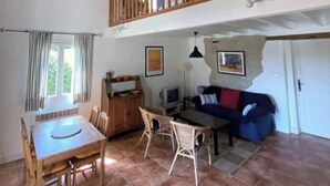 A spacious living area with a dining table, chairs, a sofa, and a TV. A balcony with wooden railings is visible above. - 1 Bedroom Private vacation home in Ronsenac (Ronsenac)