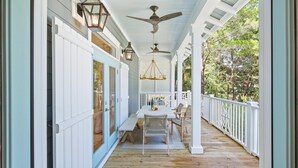 A covered porch with a wooden floor, white railings, and a table with chairs.