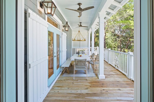 A covered porch with a wooden floor, white railings, and a table with chairs. - Seacrest Home with Pool and Wet Bar (Seacrest Beach)