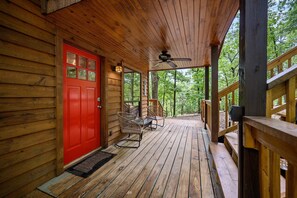 A wooden cabin with a red door, a porch with wooden railings, and a ceiling fan.