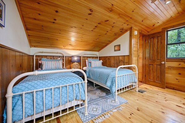 A bedroom with two bunk beds, wooden walls, a wooden ceiling, and a window.