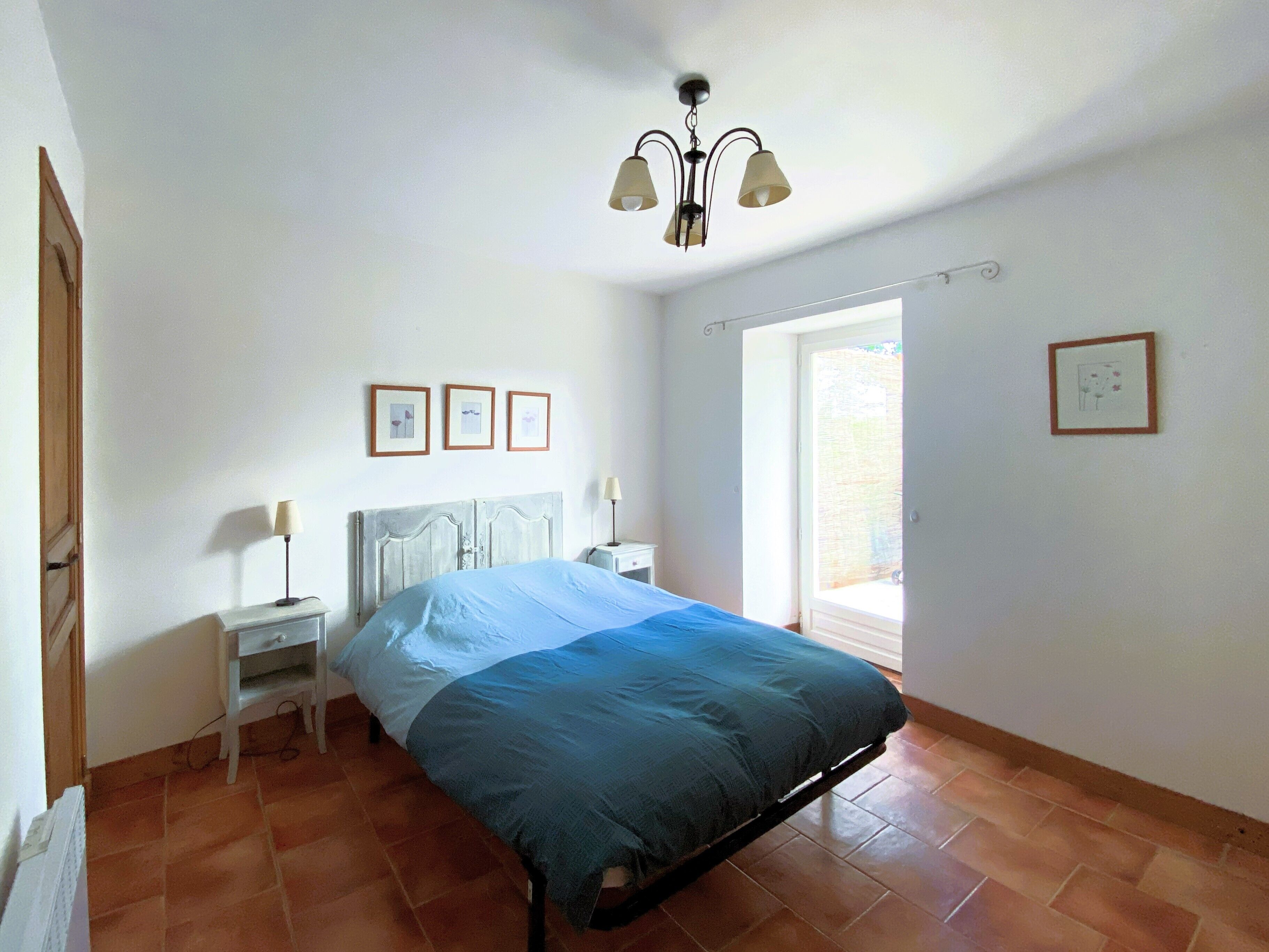 Een slaapkamer met een bed, nachtkastje, lamp, plafondlamp en raam.