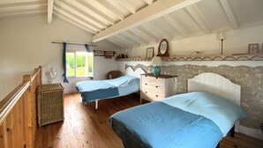 A bedroom with two beds, wooden flooring, a stone wall, and a window with curtains.