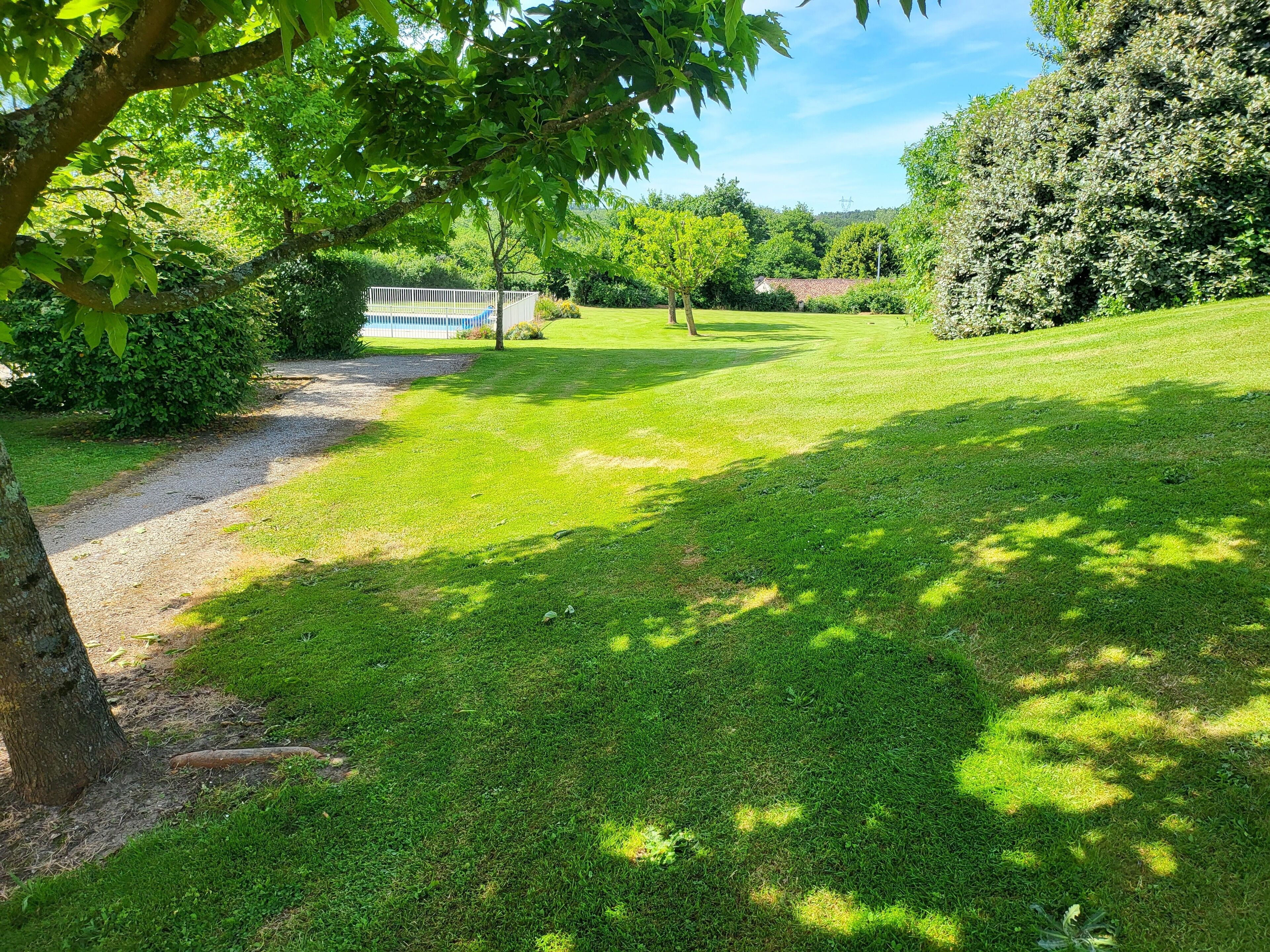 A well-maintained grassy area with a gravel path, surrounded by trees and a white fence.