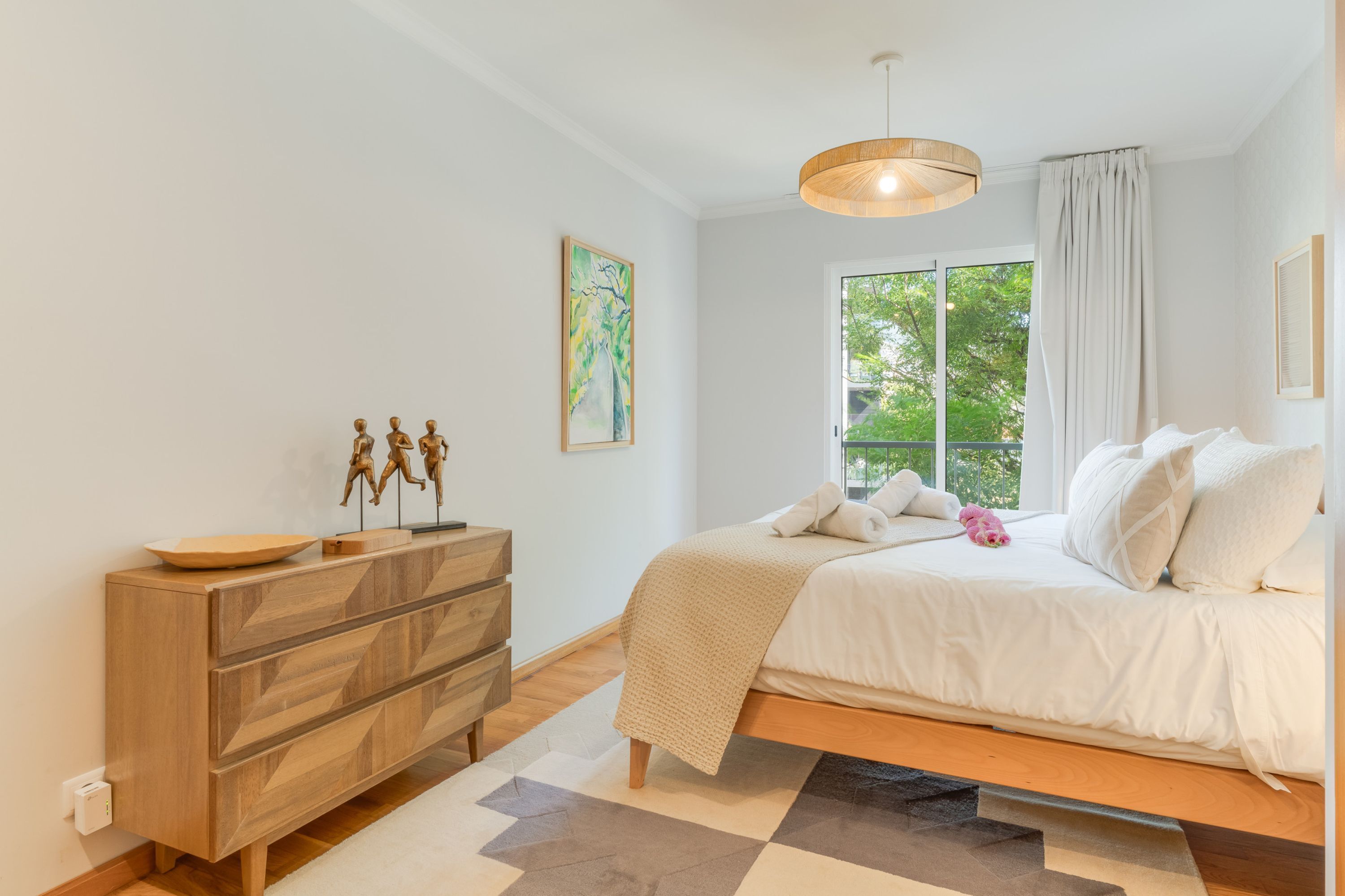 Um quarto com uma cama, cômoda, janela com cortinas e um quadro na parede.
