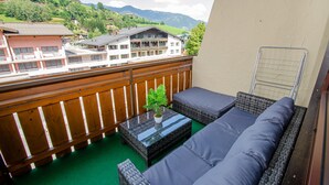A balcony with wicker furniture, a small table with a plant, and a view of buildings and mountains. - Penthouse Eightyone Kaprun Incl Summer Card (Kaprun)