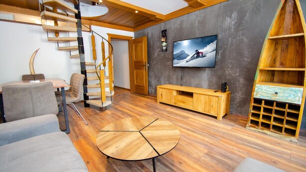 A modern living room with a spiral staircase, wooden furniture, a flat-screen TV, and a ski-themed wall decoration. - Penthouse Eightyone Kaprun Incl Summer Card (Kaprun)