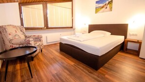A bedroom with a bed, a chair, a small table, and a window with blinds. - Penthouse Eightyone Kaprun Incl Summer Card (Kaprun)