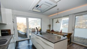 A modern kitchen with a central island, large windows, and a view of a snowy landscape. - Superb Alpine Lodges Zell am See 4pax (Zell am See)