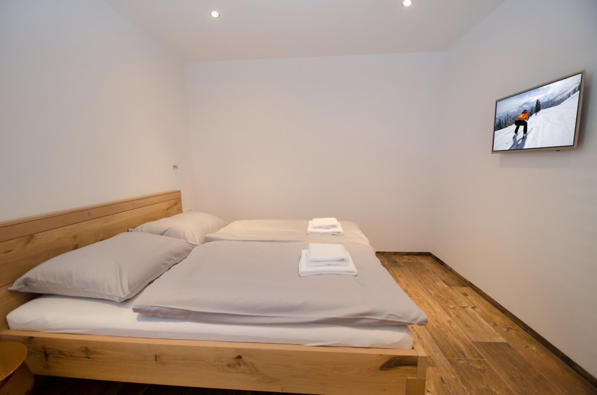 A single bed with a wooden headboard, white bedding, and a folded towel on the footboard.