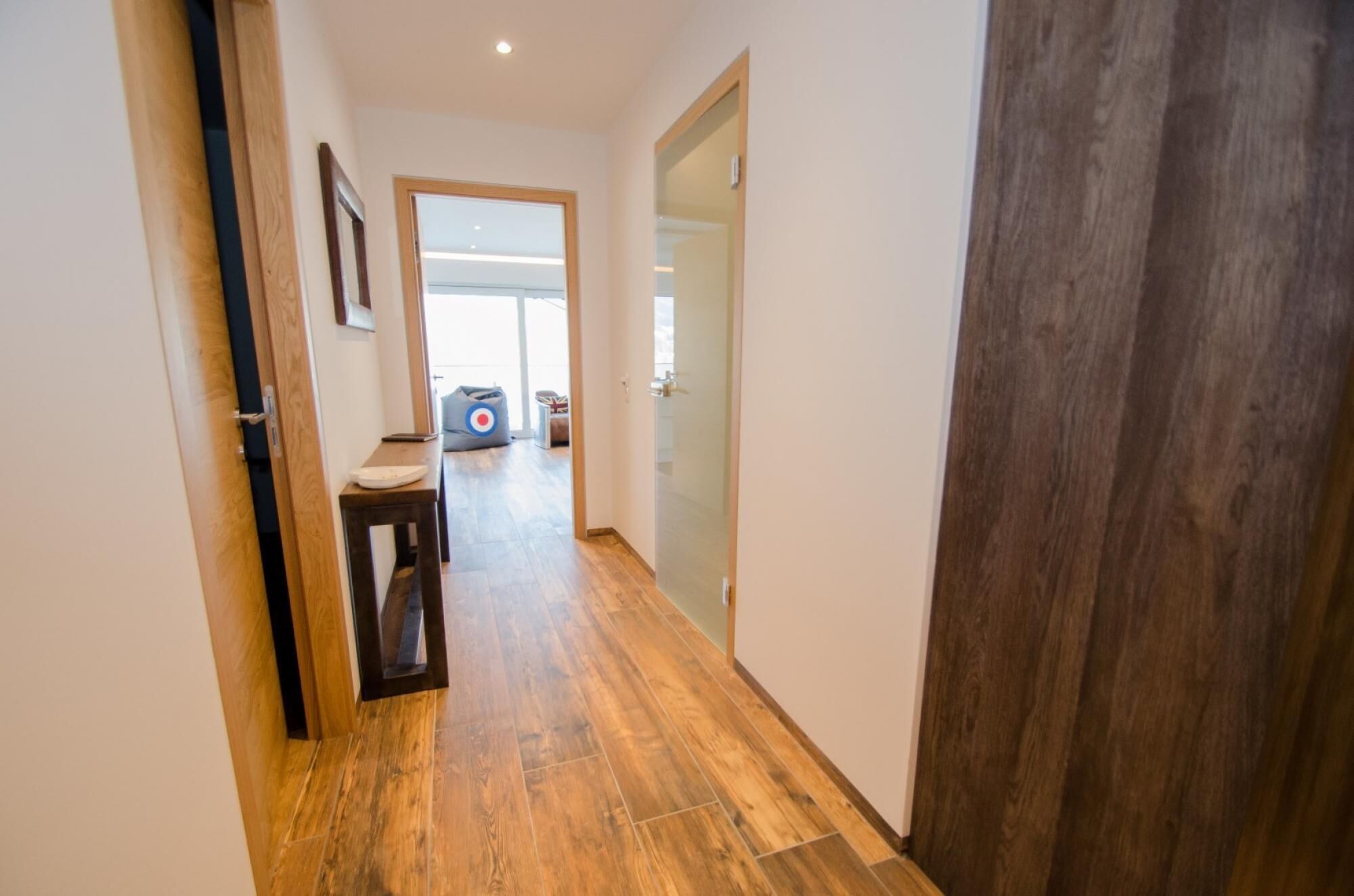 A hallway with wooden flooring, a bench, a door, and a bag in the background.