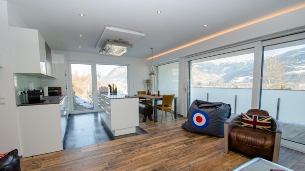 A modern interior with a kitchen, dining area, and seating space with a view of mountains. - Superb Alpine Lodges Zell am See 4pax (Zell am See)