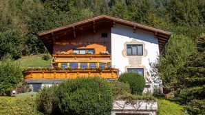 Un chalet de dos plantas con un balcón de madera, rodeado de abundante vegetación y árboles.