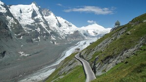 A winding mountain road with a glacier and snow-capped peaks in the background. - Panorama Apartments Bruck TOP 1 (Bruck an der Grossglocknerstrasse)