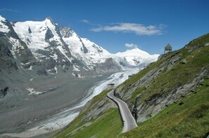 A winding mountain road with a glacier and snow-capped peaks in the background. - Panorama Apartments Bruck TOP 1 (Bruck an der Grossglocknerstrasse)