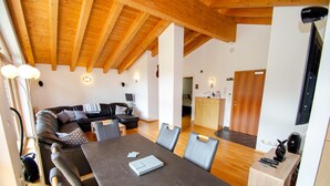 A modern living room with a wooden ceiling, a sofa, a dining table with chairs, and a kitchen area in the background. - Ski Chalet Jim 300 m From ski Lift (Zell am See)