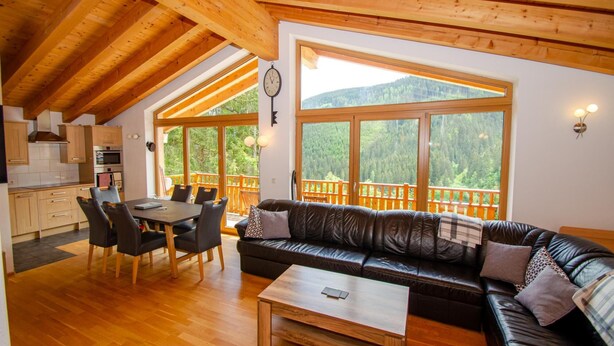 A cozy cabin interior with a dining area, a sofa, and a large window overlooking a forested mountain. - Ski Chalet Jim 300 m From ski Lift (Zell am See)