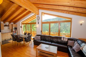 A cozy cabin interior with a dining area, a sofa, and a large window overlooking a forested mountain. - Ski Chalet Jim 300 m From ski Lift (Zell am See)