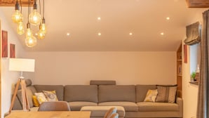 A cozy living room with a wooden ceiling, a sofa, a dining table, and hanging light fixtures. - Finest Villa Zell am See Luxury Sauna 12 pax (Zell am See)
