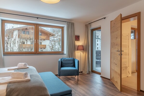 Una habitación de hotel moderna con un ventanal grande, un sofá azul, una puerta de madera y una lámpara.