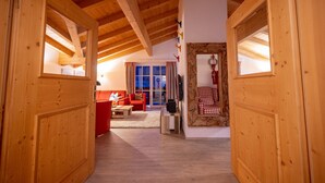 Een houten interieur met een hoge plafond, een rode bank, een geruit stoel en een stenen openhaard.