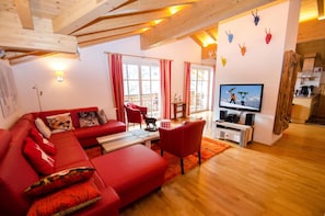 Een gezellige woonkamer met een rode bank, een televisie en een houten plafond.