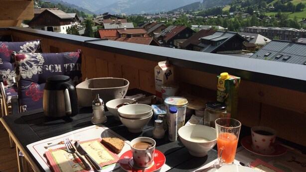 Een balkon met een ontbijttafel, inclusief een koffiekop, sap en een bord eten.