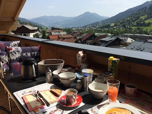 A balcony with a table set for breakfast, including a coffee cup, juice, and a plate of food. - Finest Penthouse All Seasons Lodge Kaprun (Kaprun)