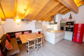 Een moderne keuken met houten balken, een eethoek met een houten tafel en stoelen, en een rode koelkast.