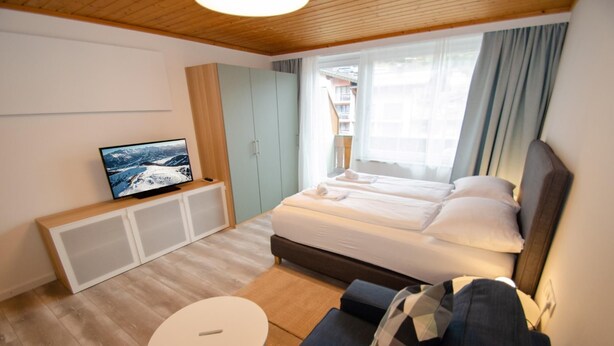 A modern hotel room with a large bed, a television on a cabinet, a small round table, and a sofa. - Deluxe Studio Kaprun TOP 72 (Kaprun)