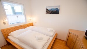 A bedroom with a wooden bed, a window with curtains, a wall-mounted picture, and a wooden cabinet. - Panorama Apartments Bruck TOP 2 (Bruck an der Grossglocknerstrasse)