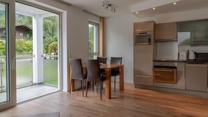 A modern kitchen with stainless steel appliances, a dining area with a wooden table and chairs, and large sliding glass doors leading to a balcony with a view of greenery. - Apartment Glacier View 12 1 With Balcony (Kaprun)