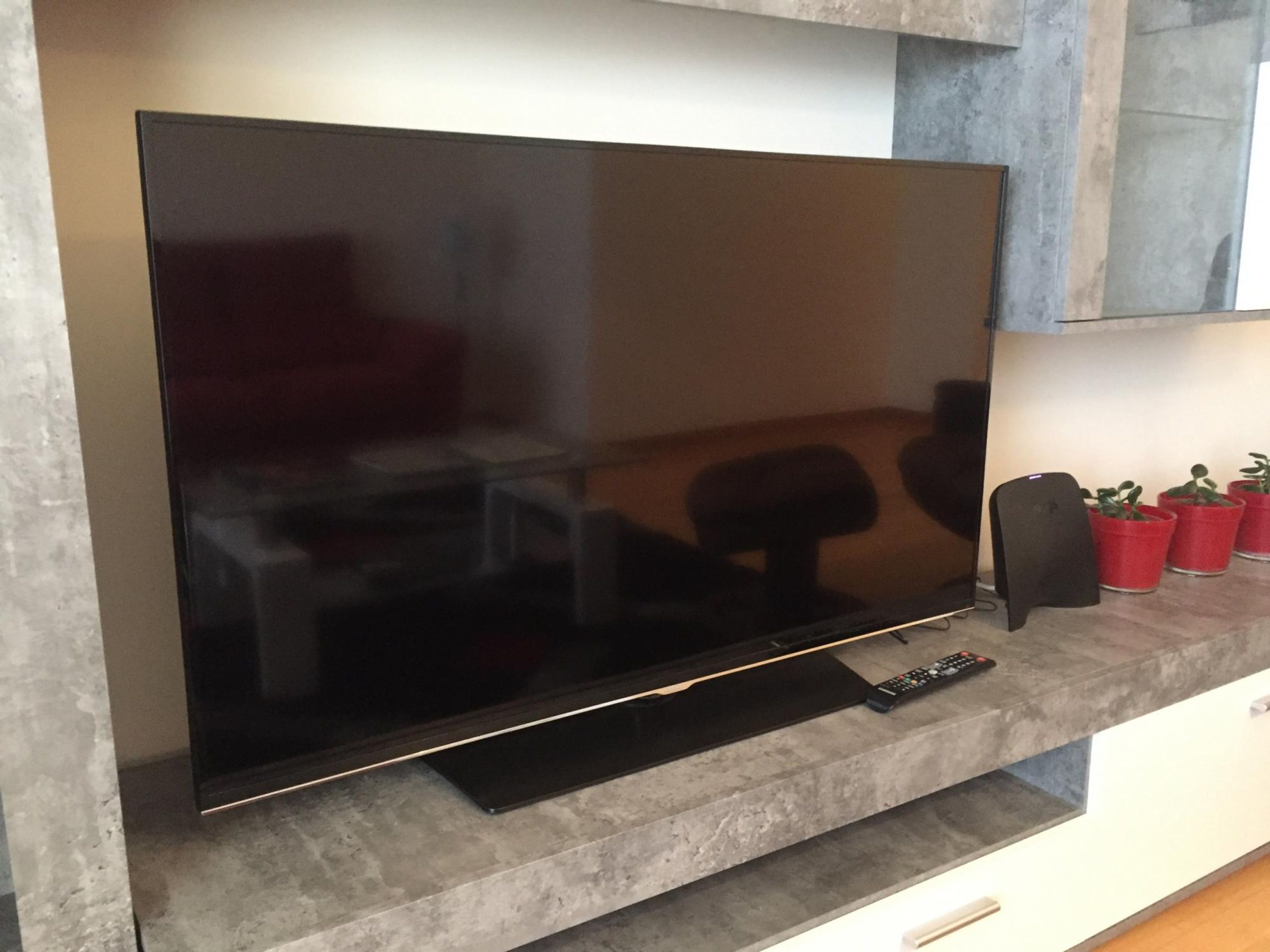 A flat-screen TV mounted on a wall with a remote control on a shelf below.