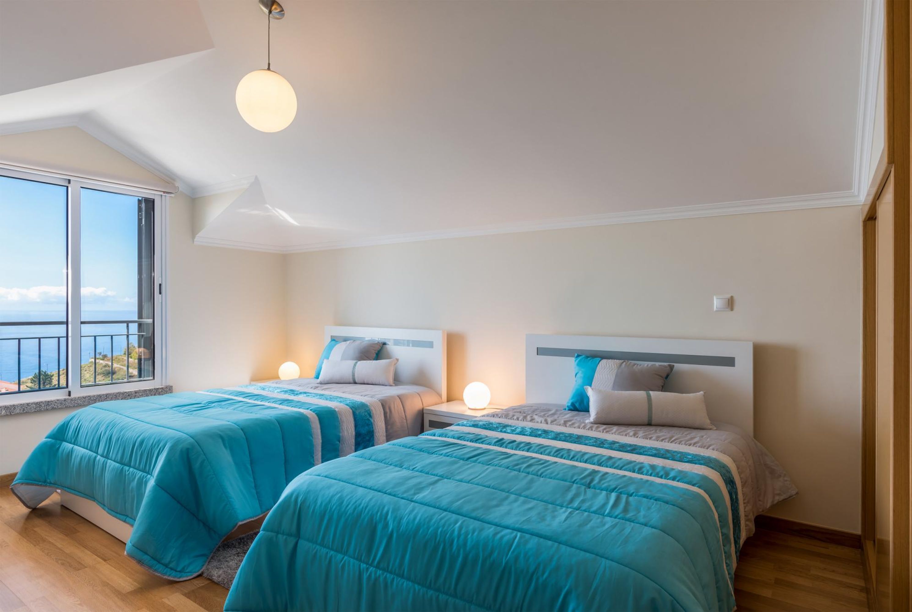 A bedroom with two beds, a large window, and a view of the sea.