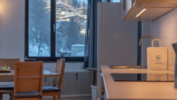 A modern kitchen with a window view, a dining area with a table and chairs, and a bag on the counter.