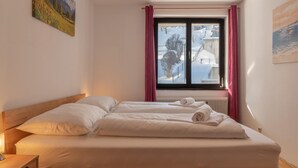 A double bed with white linens and a view of a snowy landscape through a window.