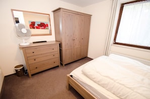 Quarto com cama, cómoda, guarda-roupa, ventoinha e janela com cortinas.