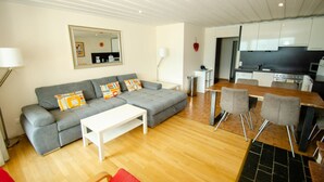 Una sala de estar moderna con un sofá gris, una mesa de centro blanca y un comedor con una mesa de madera y cuatro sillas.