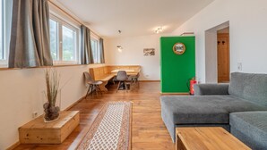 En stue med en grå sofa, et træbord og et spiseområde med en bænk og stole.