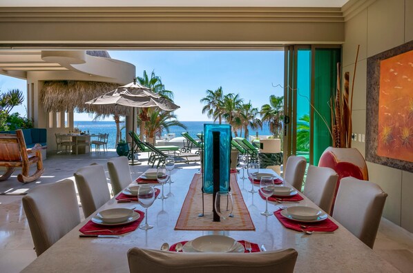 Un espace repas avec vue sur l’océan, un parasol en chaume et une table dressée pour le repas.