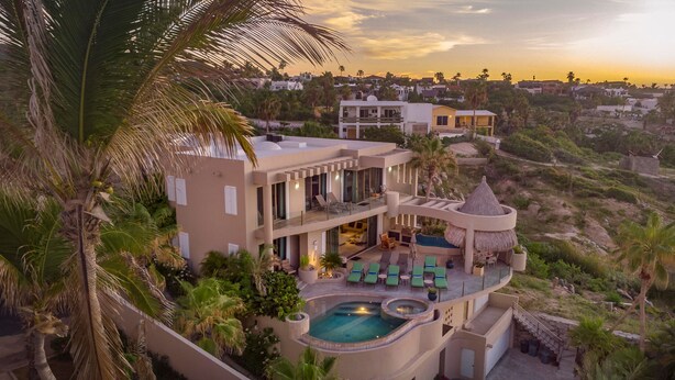A modern multi-story house with a pool, outdoor seating, and palm trees.