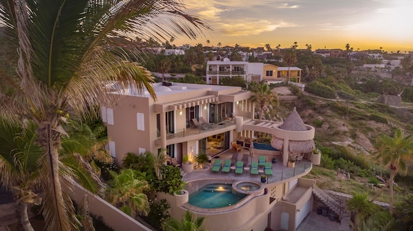 A modern multi-story house with a pool, outdoor seating, and palm trees.