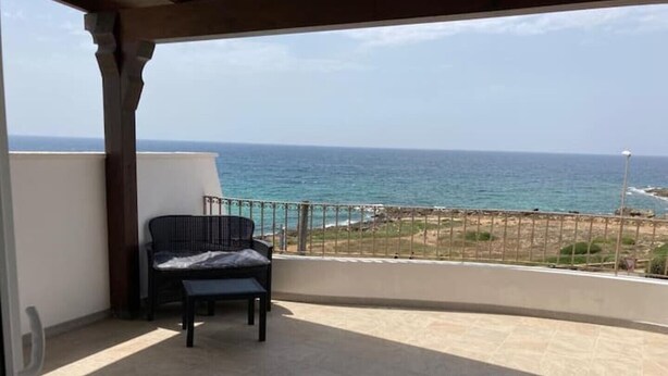Un balcon avec vue sur la mer, une chaise et une petite table.