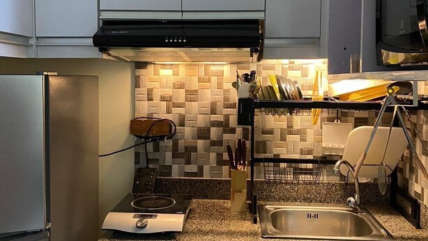 Een kleine keuken met witte kastjes, een zwarte afzuigkap, een decoratieve spatwand en een granieten aanrecht.