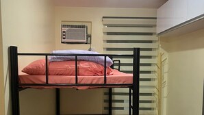 Een slaapkamer met stapelbed, plafondventilator, radiator en een klein krukje.