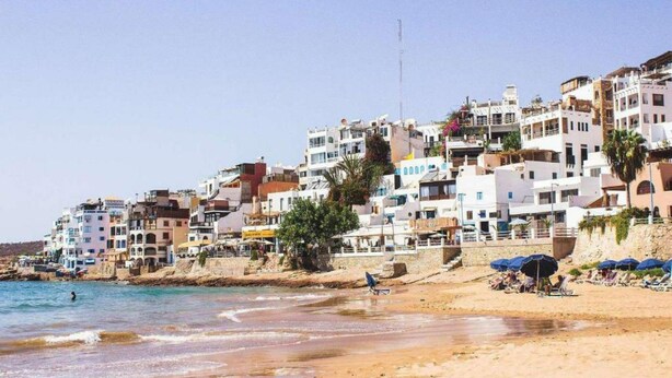 Une ville côtière avec des immeubles à plusieurs étages, une plage de sable et un ciel dégagé.