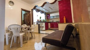 Un salon comprenant un canapé, une table à manger et des chaises. Il y a également un coin cuisine avec des placards rouges et une vue sur l’extérieur.