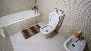 Une salle de bain avec une baignoire, des toilettes, un bidet et un petit tapis.
