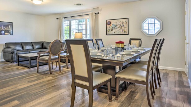 Un comedor con una mesa de madera dispuesta para cuatro personas, rodeada de sillas. Se ve un sofá y una mesa auxiliar al fondo.