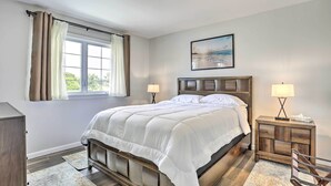 Un dormitorio con una cama grande, dos mesitas de noche con lámparas, un cabecero de madera, una ventana con cortinas y un cuadro en la pared.